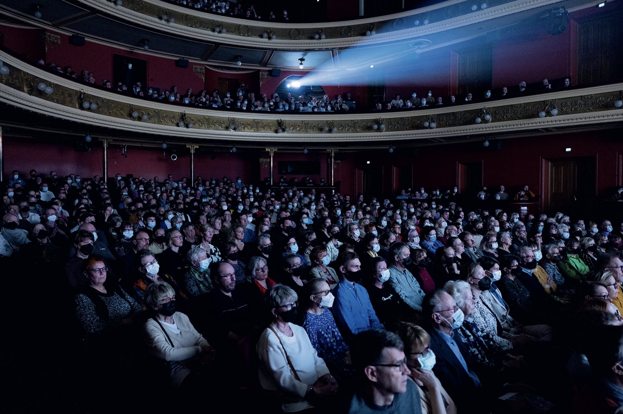 Full theatre of seated audience members, many in masks, watching a Black Box performance