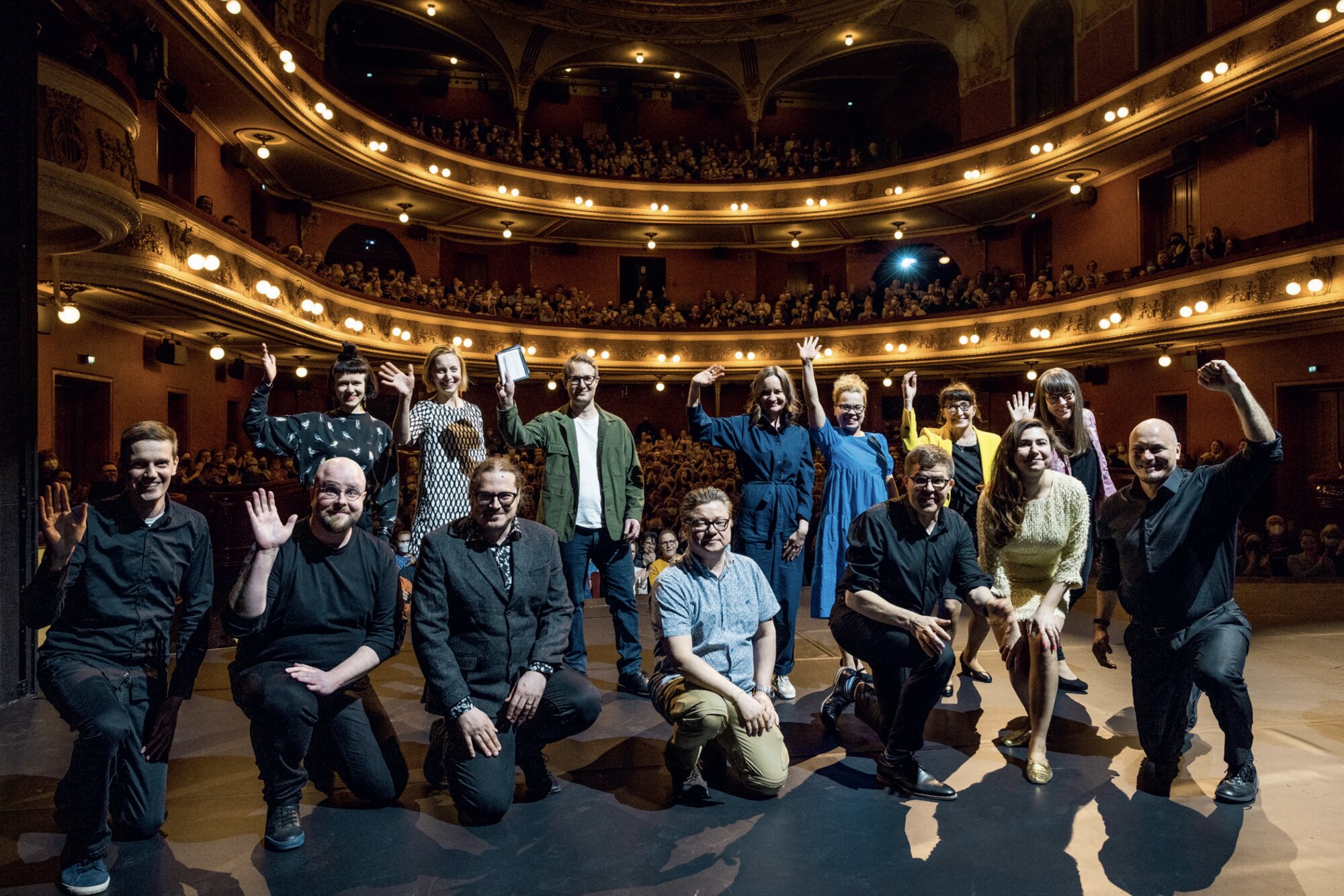 Black Box production team posing and waving on the Finnish National Theatre stage before a full house